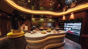 Un área de bar moderna con una barra curva, una zona de estar con un sofá amarillo y un refrigerador con bebidas.
