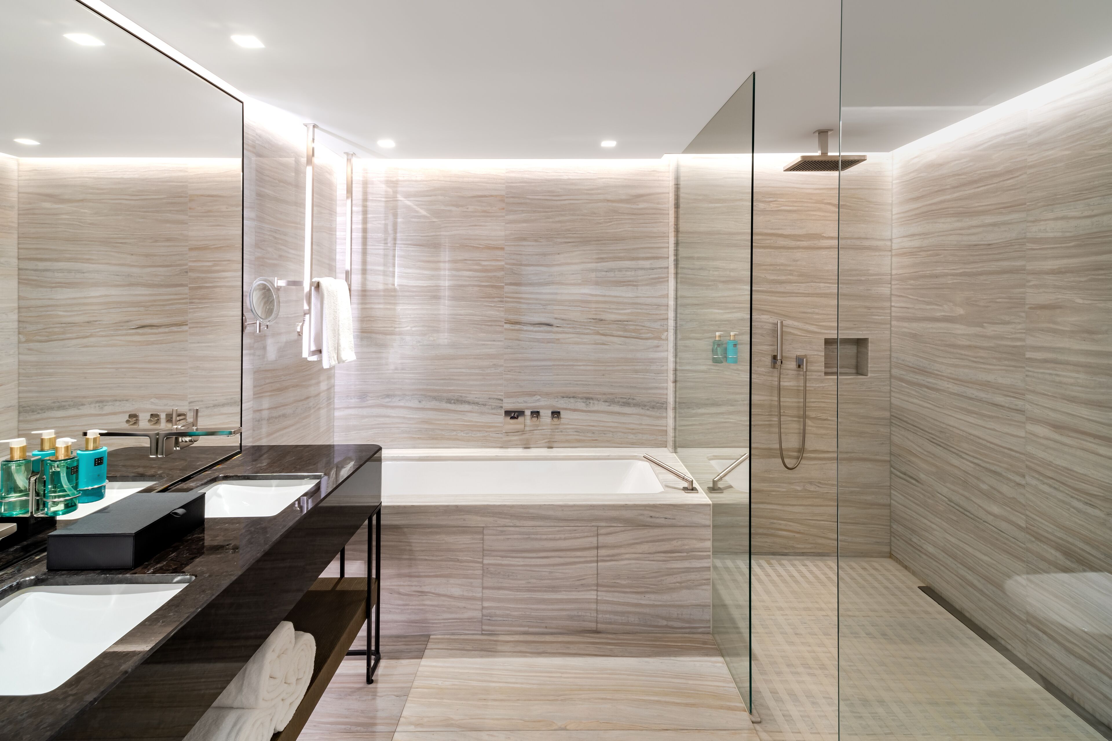 Une salle de bain moderne dotée d’une grande baignoire, de deux lavabos, d’une douche à parois de verre et d’un meuble-lavabo avec des articles de toilette.