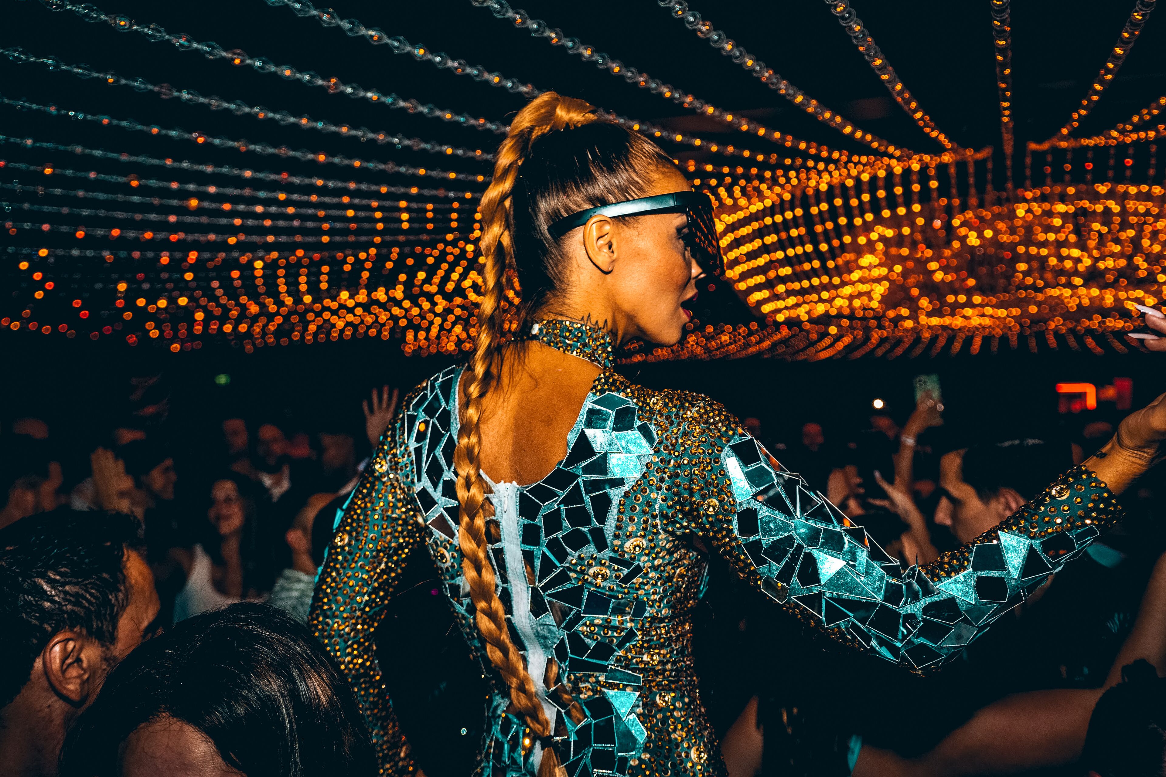 Una persona con un atuendo estampado en un evento concurrido, bajo un techo lleno de luces.