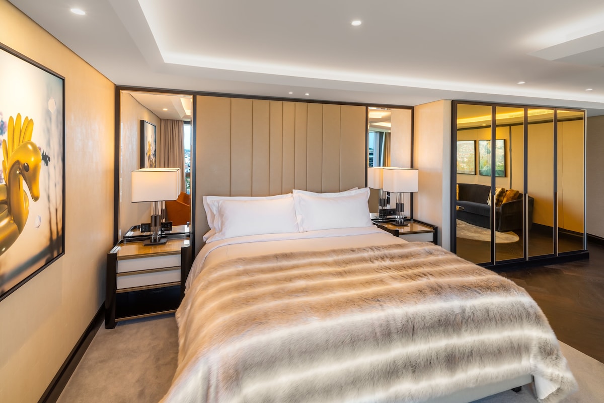 Een moderne hotelkamer met een groot bed, nachtkastjes, een spiegel en uitzicht door een schuifdeur.