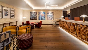 A modern lobby with a wooden floor, leather armchairs, a red sofa, and abstract wall art.