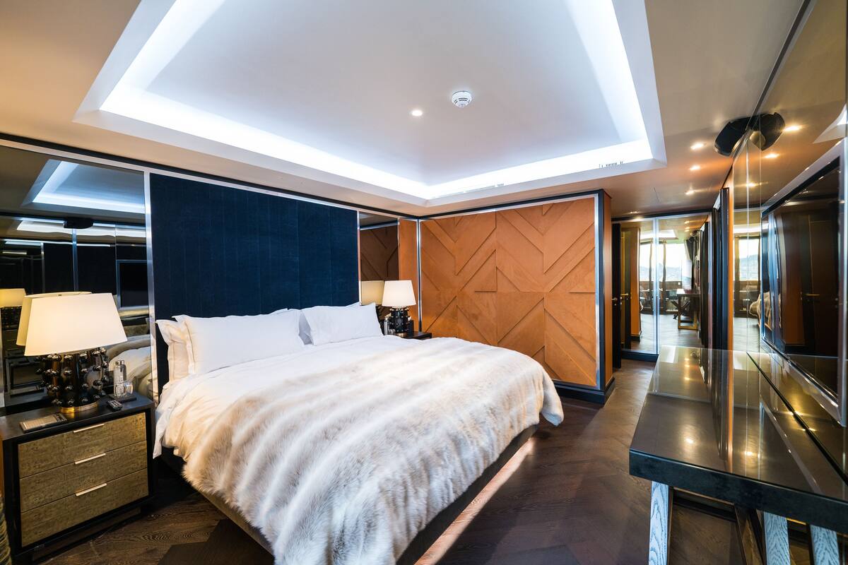 A modern hotel room with a large bed, a nightstand with a lamp, a wooden accent wall, and a large mirror.