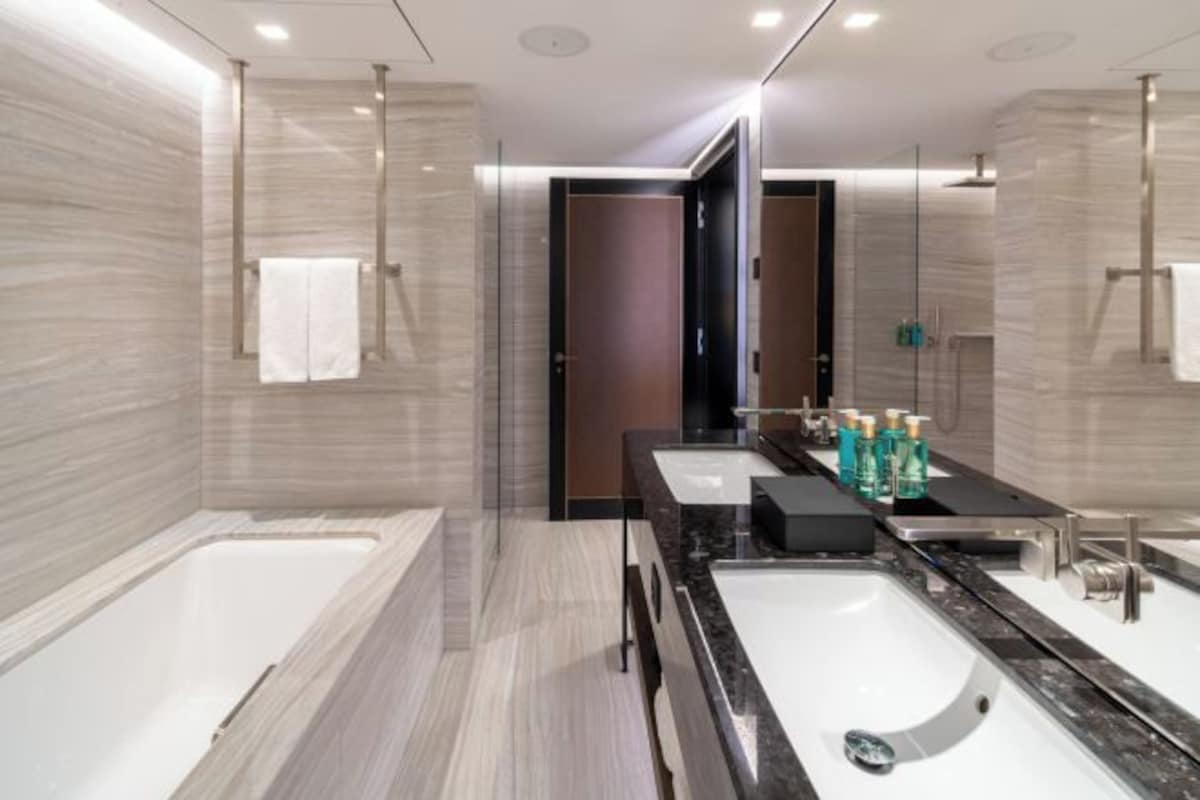 A modern bathroom with a large bathtub, two sinks, and a dark wooden door.
