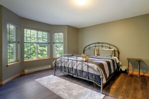 A bedroom with a bed, windows, a radiator, and a small table.
