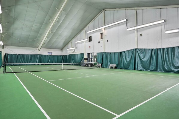 An indoor tennis court with a net, green flooring, and white walls.