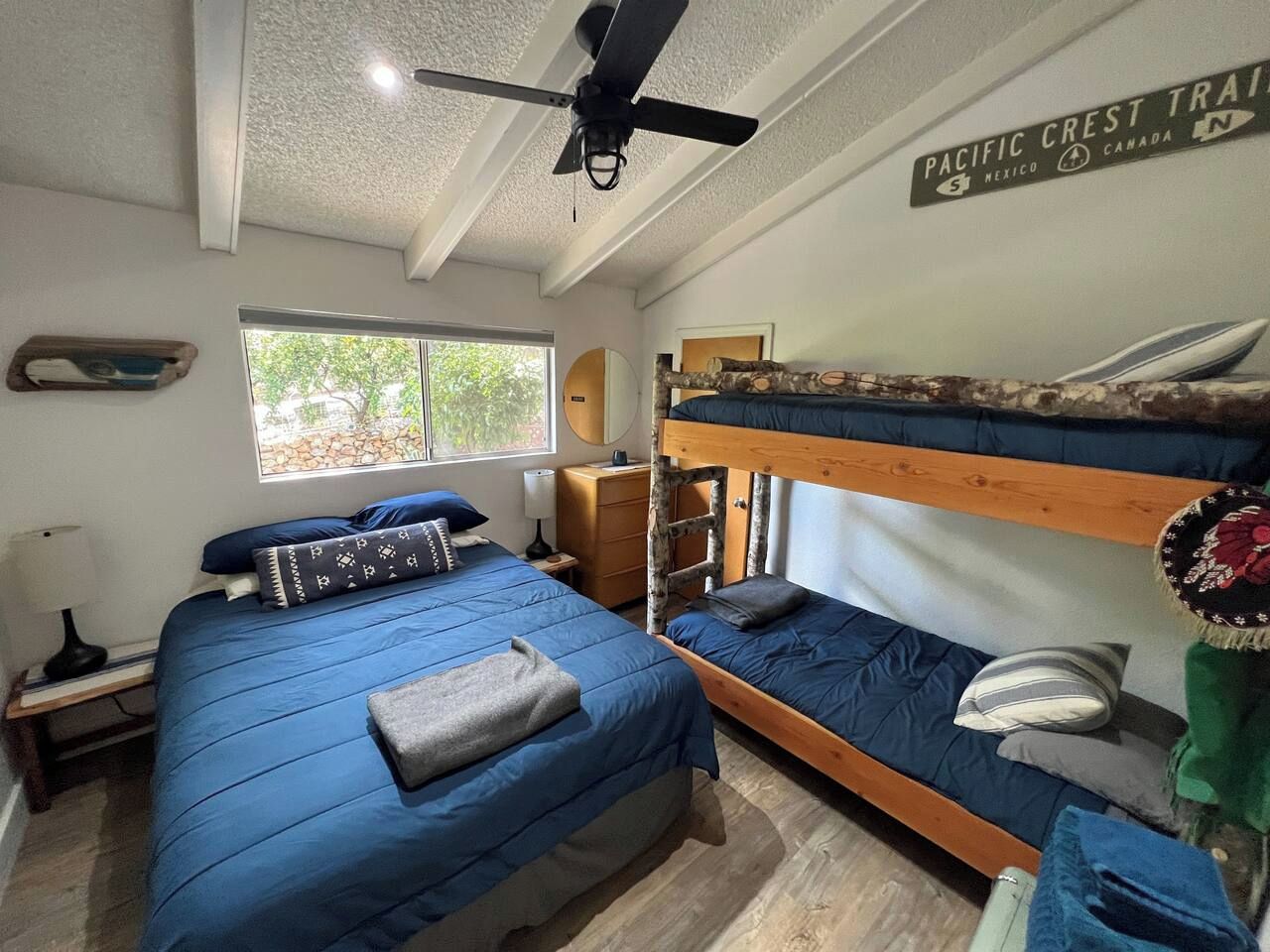 Quarto com duas camas beliche, um ventilador de teto, uma janela com vista e uma placa indicando a Trilha da Crest do Pacífico.
