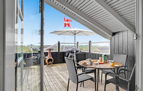 Une terrasse extérieure couverte, équipée d’une table et de chaises, d’un barbecue et offrant une vue sur la campagne.