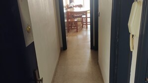 Un couloir étroit, dont le sol est recouvert de carreaux, mène à une salle à manger équipée d’une table et de chaises.