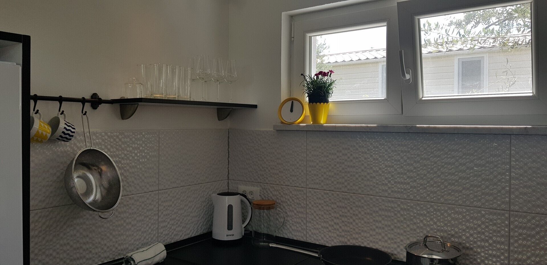 Una cocina con ventana, repisas con utensilios de cocina y una planta en maceta.