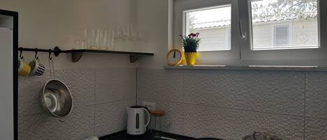 Una cocina con ventana, repisas con utensilios de cocina y una planta en maceta.