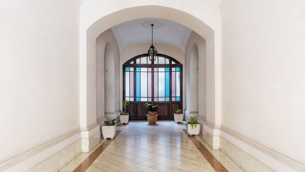 A hallway with a tiled floor, white walls, and a large arched window with a stained glass design. - GuestHost - Vatican museums cozy apt x6 (Roma)