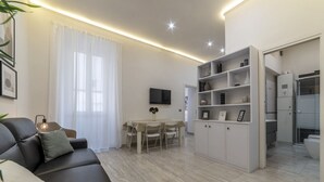 A modern living room with a sofa, a dining table, and a kitchen area with cabinets and a TV. - GuestHost - Vatican museums cozy apt x6 (Roma)