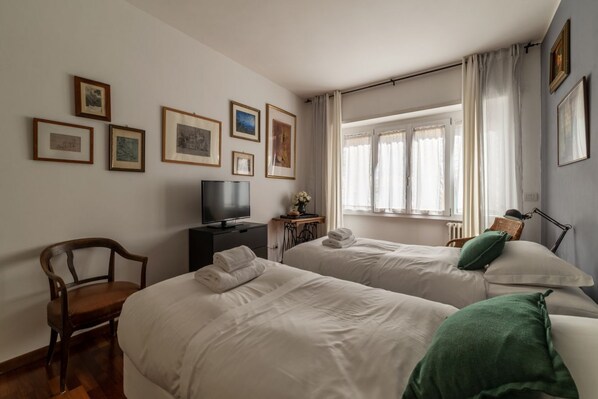 Una camera d'albergo con due letti, una televisione, una sedia e una finestra con tende.