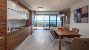 Uma cozinha moderna com uma ilha grande, uma área de jantar com mesa e cadeiras de madeira, e vista para o mar através de grandes janelas.