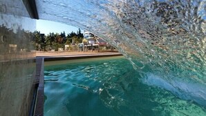Uma piscina com água cristalina, rodeada por uma área de lazer com espreguiçadeiras e um edifício ao fundo.
