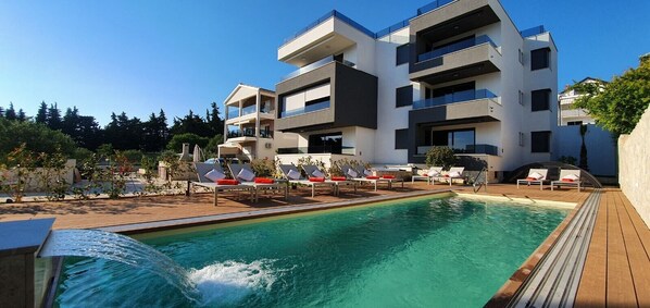 A modern building with a pool and sun loungers.