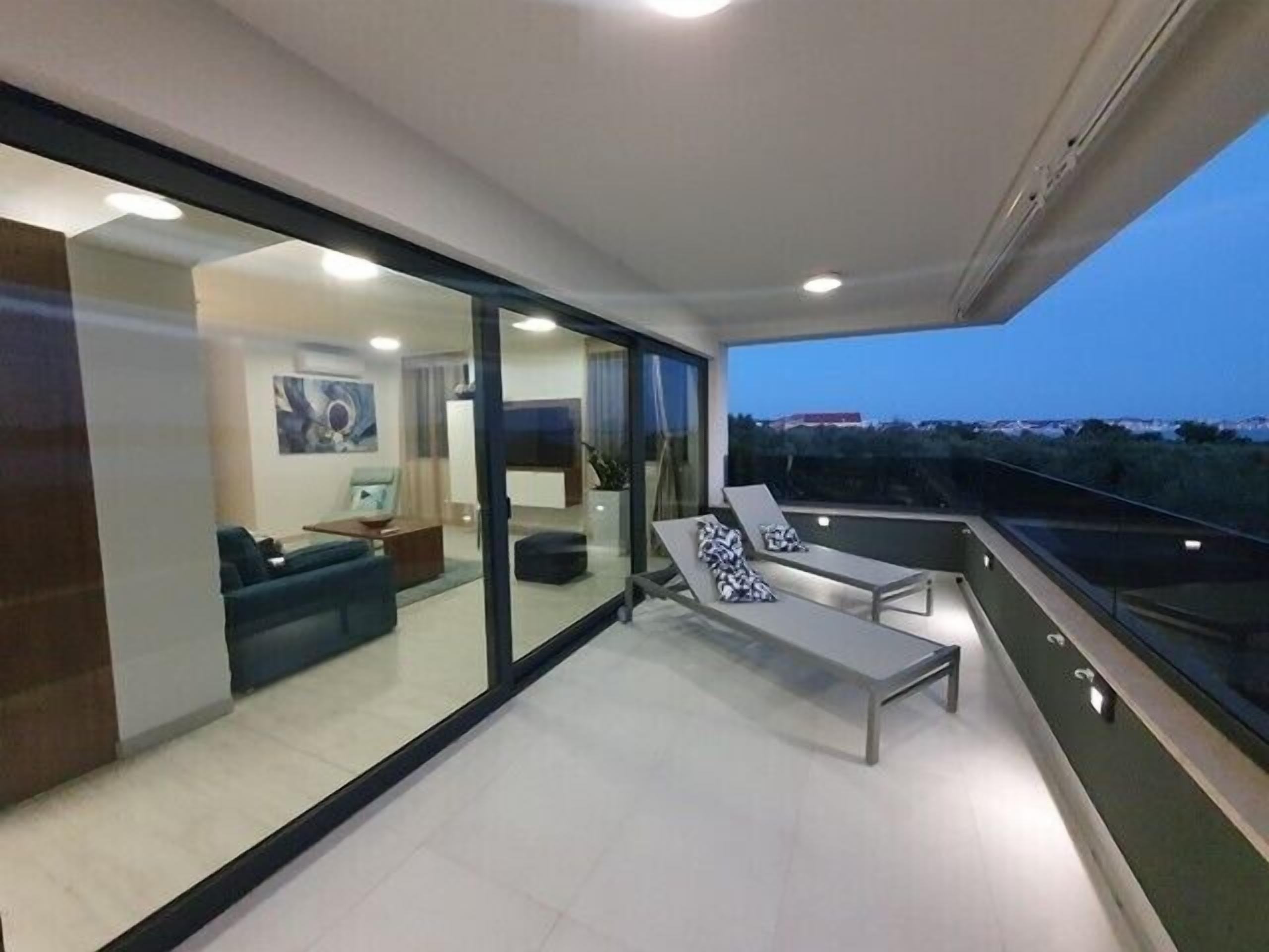 Ein modernes Wohnzimmer mit einer Glaswand, einem Balkon mit zwei Liegestühlen und Blick auf die Landschaft.