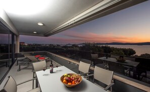 Un área de comedor moderna al aire libre con vista al atardecer sobre el agua.