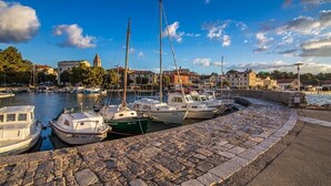 A marina with boats docked, a stone walkway, and buildings in the background.
