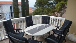 A balcony with a round table and six chairs, surrounded by a white balustrade.