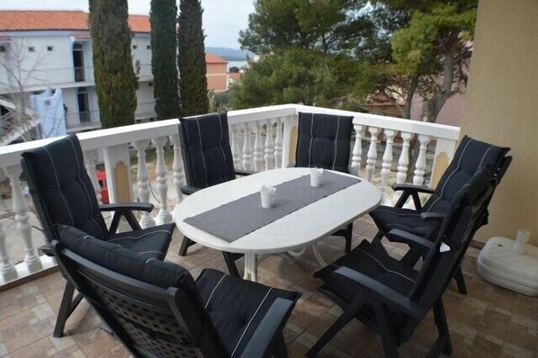 A balcony with a round table and six chairs, surrounded by a white balustrade.