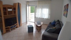 A living room with a sofa, a coffee table, a TV on a wooden stand, and a sliding glass door leading to an outdoor area.