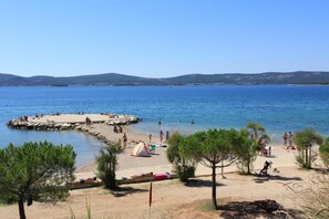Une plage où des gens se prélassent au soleil et se baignent, un petit quai et des pins.