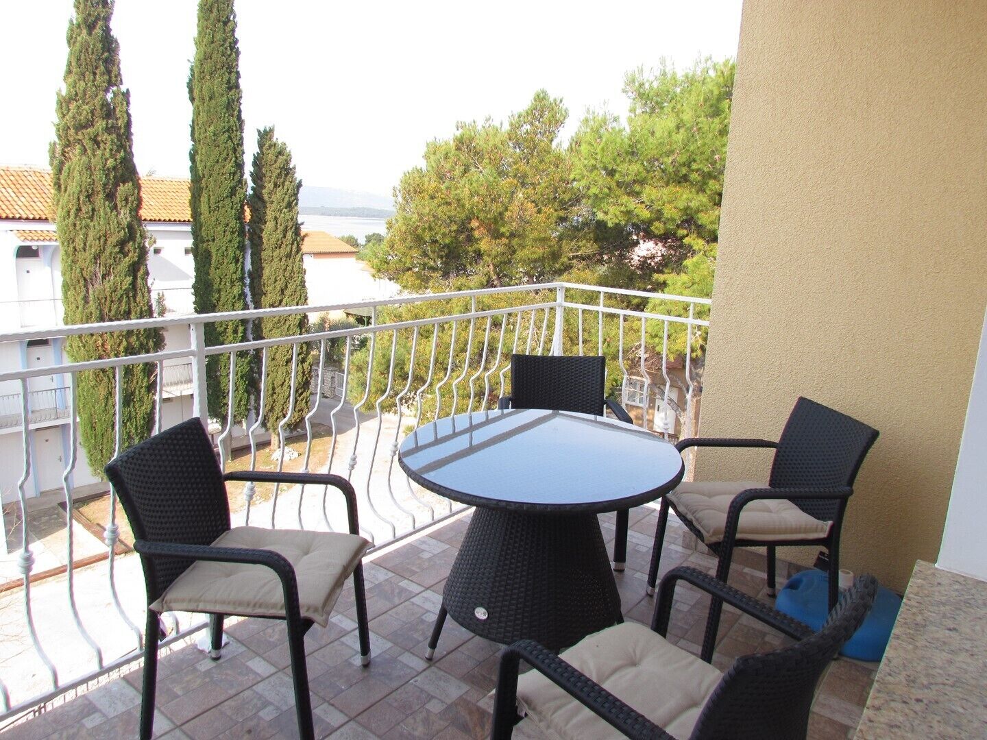Varanda com mesa redonda e quatro cadeiras, com vista para uma área residencial com árvores e casas.