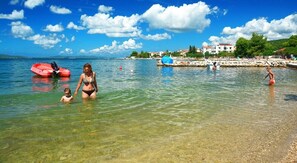 A clear beach with people swimming and a red inflatable boat in the water.