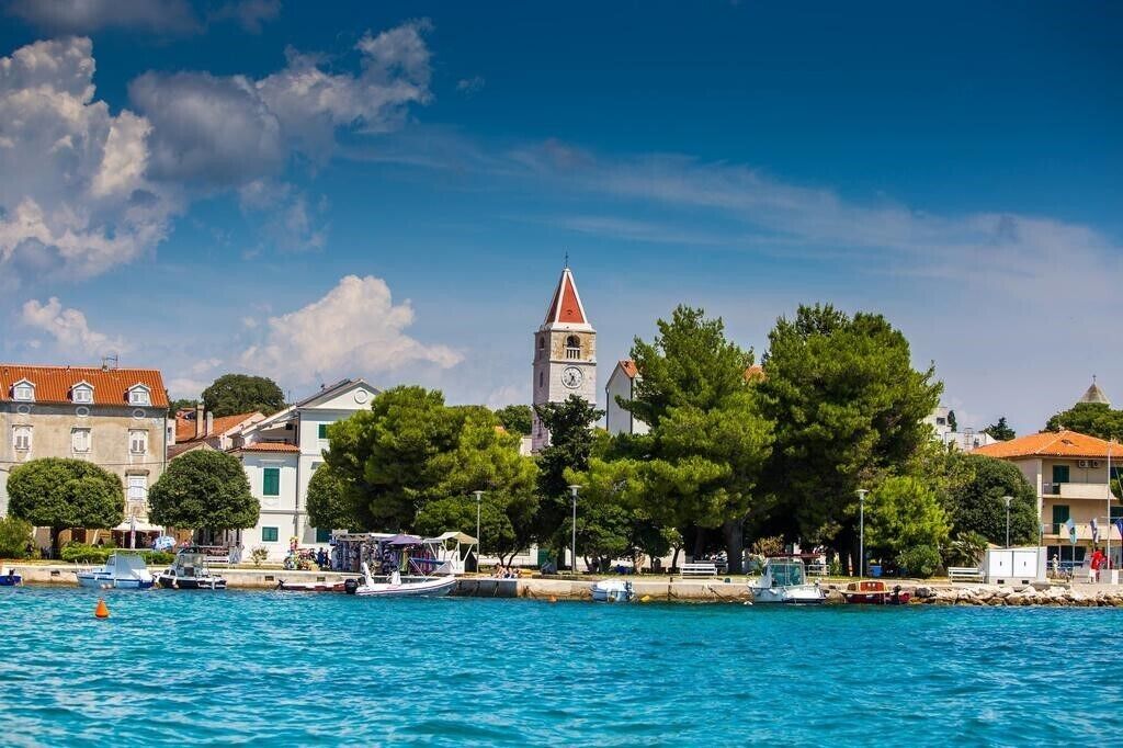 A coastal town with a prominent church tower, waterfront buildings, and boats docked along the shore.