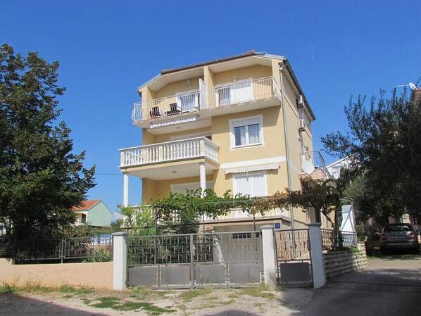 A multi-story residential building with balconies, a gated entrance, and a clear sky.