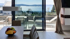 A modern dining area with a table set for two, a bowl of fruit, and a view of a body of water and hills. - Villa Ivan two bedroom apartment with sea view (Sv. Filip I Jakov)