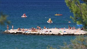 A beach with people sunbathing and swimming, boats in the water, and a rocky pier. - Villa Ivan two bedroom apartment with sea view (Sv. Filip I Jakov)