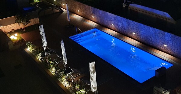 An outdoor swimming pool with a stone wall and a wooden deck.