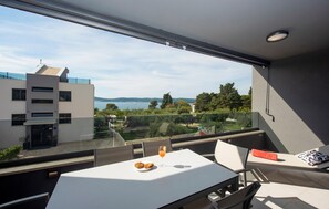 A balcony with a table, chairs, and a glass railing overlooking a scenic view of buildings and trees.