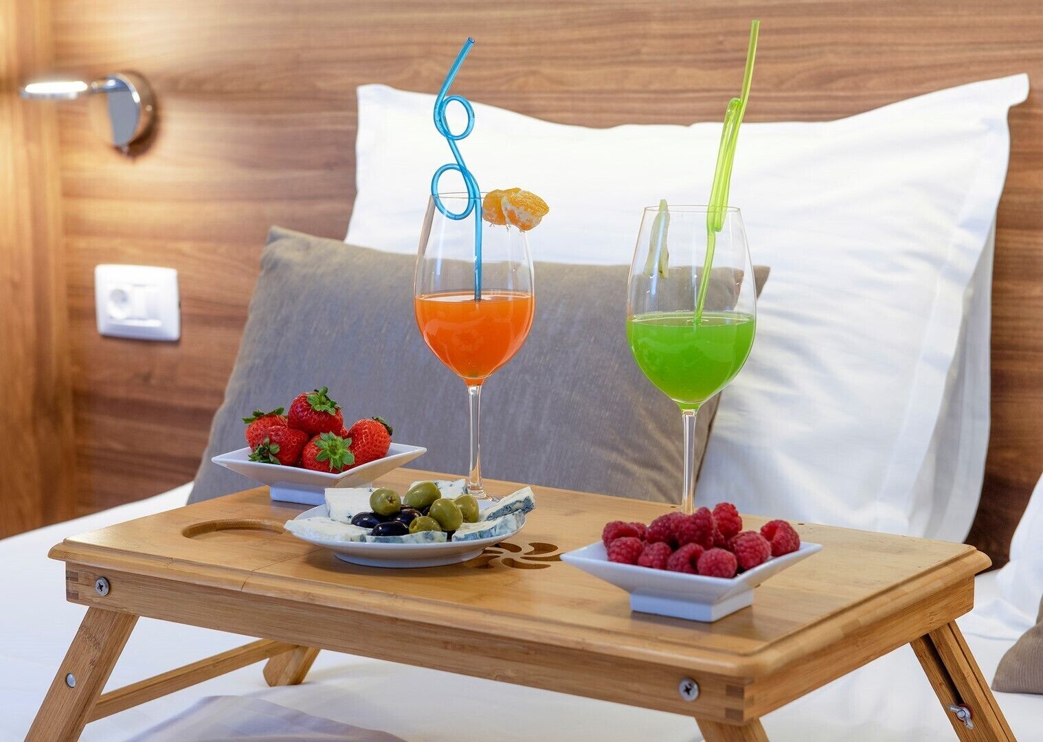 Un plateau en bois avec deux verres de cocktails, une assiette de fraises, une assiette d’olives et une assiette de framboises, le tout disposé sur une nappe.
