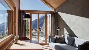 A modern room with a wooden table, a sofa, and a large window offering a mountain view.