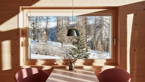A wooden cabin interior with a large window, two red chairs, a table, and a hanging pendant light.