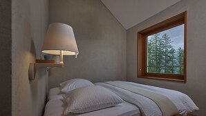 A bedroom with a bed, a bedside lamp, a window with a view of trees, and a wooden headboard.