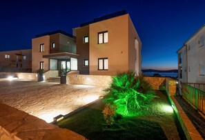 A modern hotel with a stone facade, a well-lit entrance, and a view of the sea.