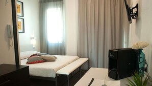 Hotelkamer met een bed, bureau, telefoon, verwarming en raam met gordijnen.