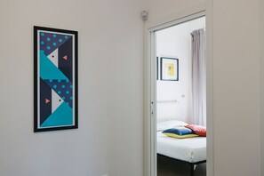 A room with a bed, a framed abstract artwork on the wall, and a framed picture of a fly on the wall.