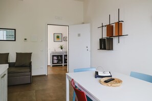 Una sala de estar moderna con un sofá blanco, una mesa de comedor con sillas, y una cocina al fondo.