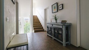 Un couloir avec un escalier, un banc, une étagère ornée d’une plante et des tableaux encadrés accrochés au mur.