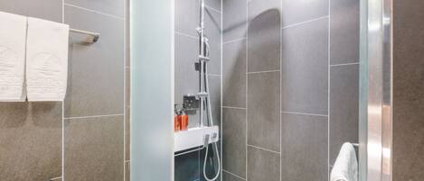 A modern bathroom with a glass shower enclosure, grey tiles, and a towel rack with a white towel.