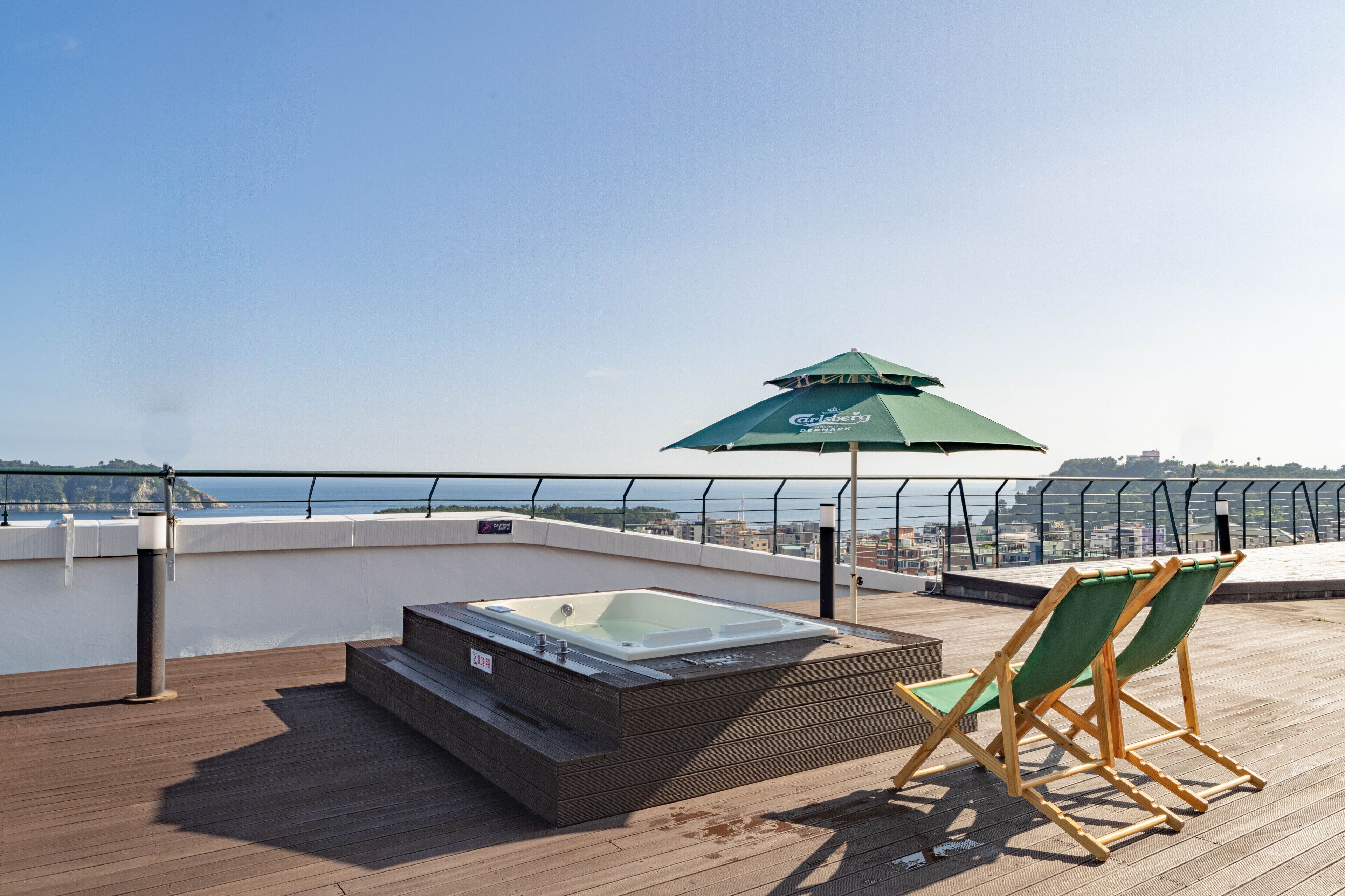 A rooftop terrace with a hot tub, two green deck chairs, and a green umbrella.