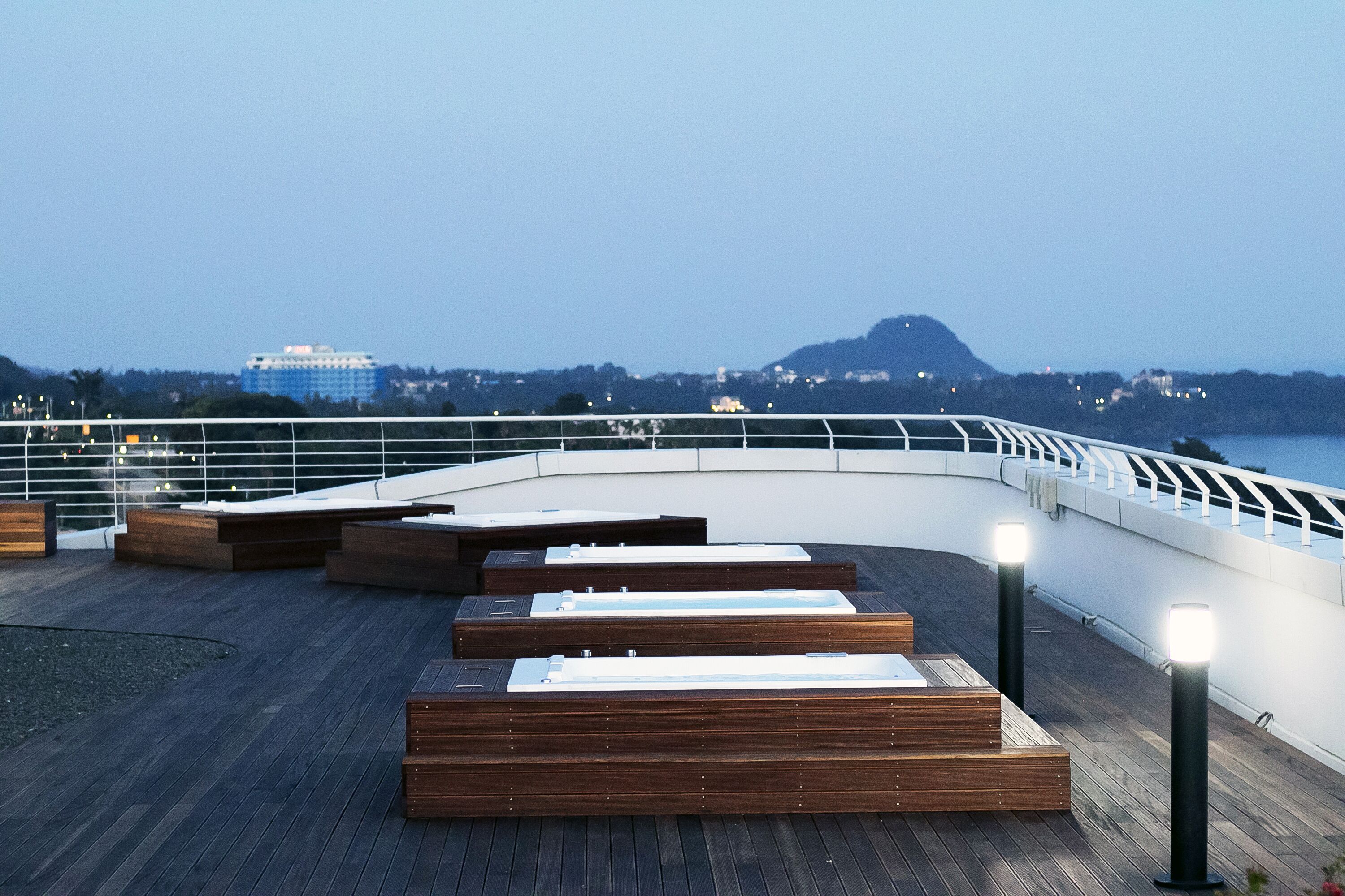 A wooden deck with seating areas and a railing overlooking a body of water and distant buildings.
