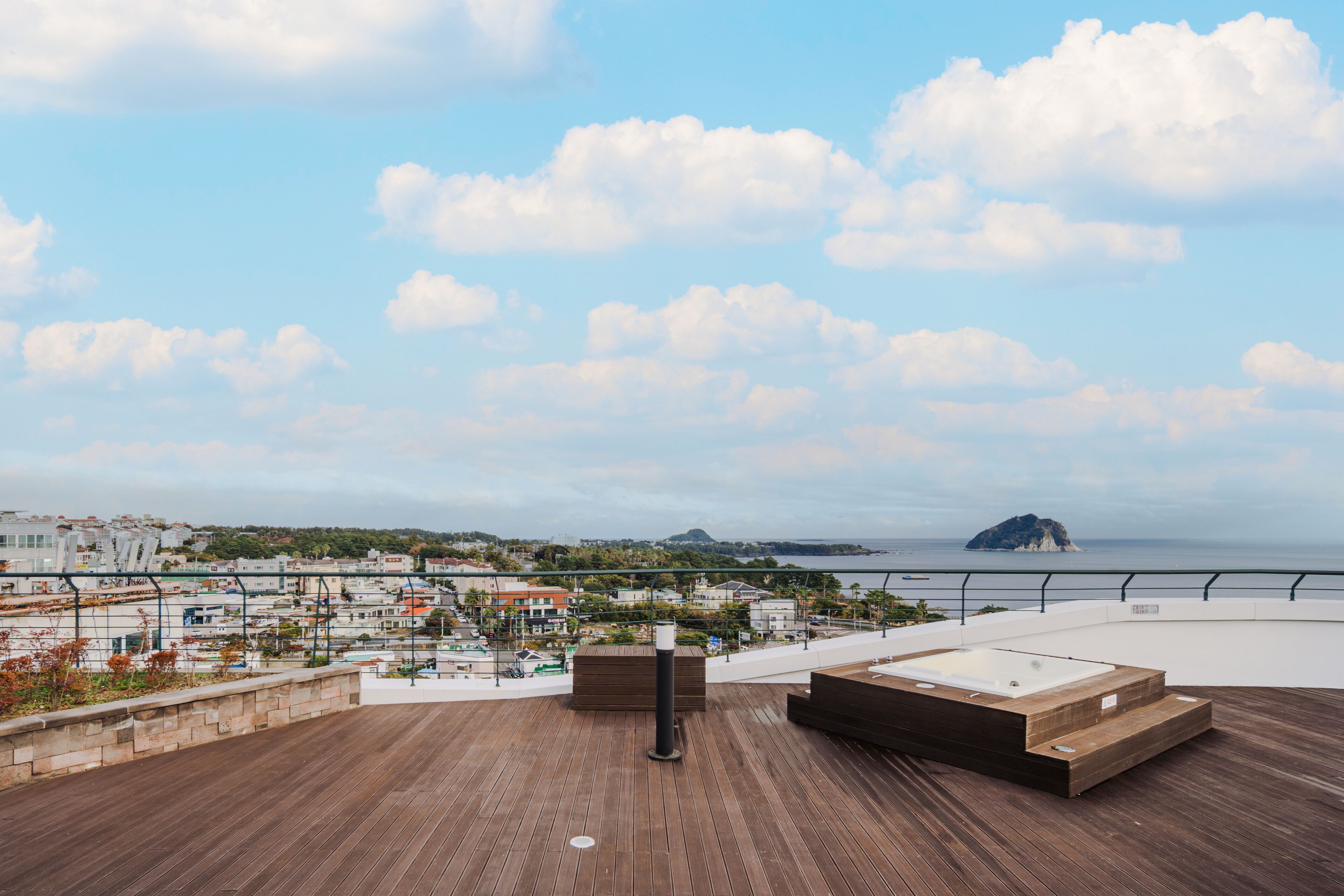 A rooftop terrace with a wooden deck, a hot tub, and a view of the sea and distant island.