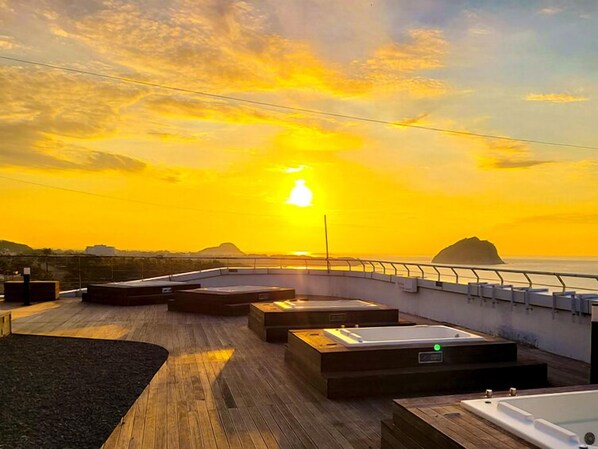 A rooftop terrace with wooden flooring, seating areas, and a view of the sunset over the ocean. - Hotel Bridge Seogwipo (Seogwipo)