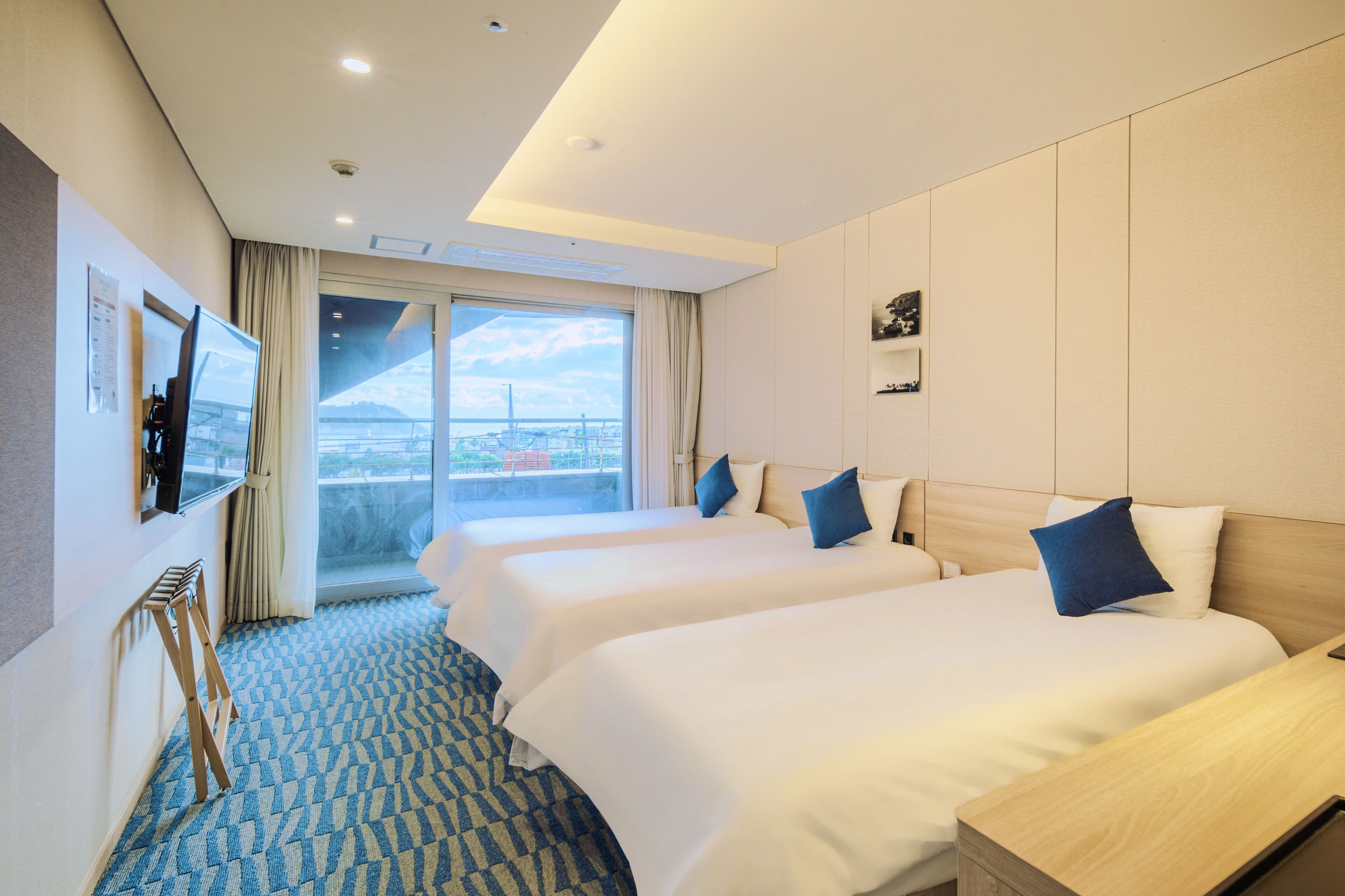 A hotel room with two beds, a TV, and a large window with a city view.